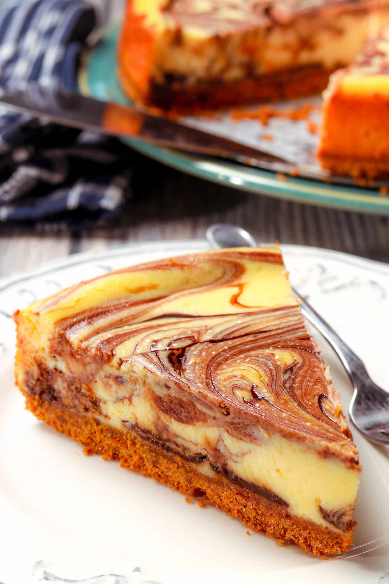 slice of hot fudge marble cheesecake on a plate with a pan of cheesecake in the background