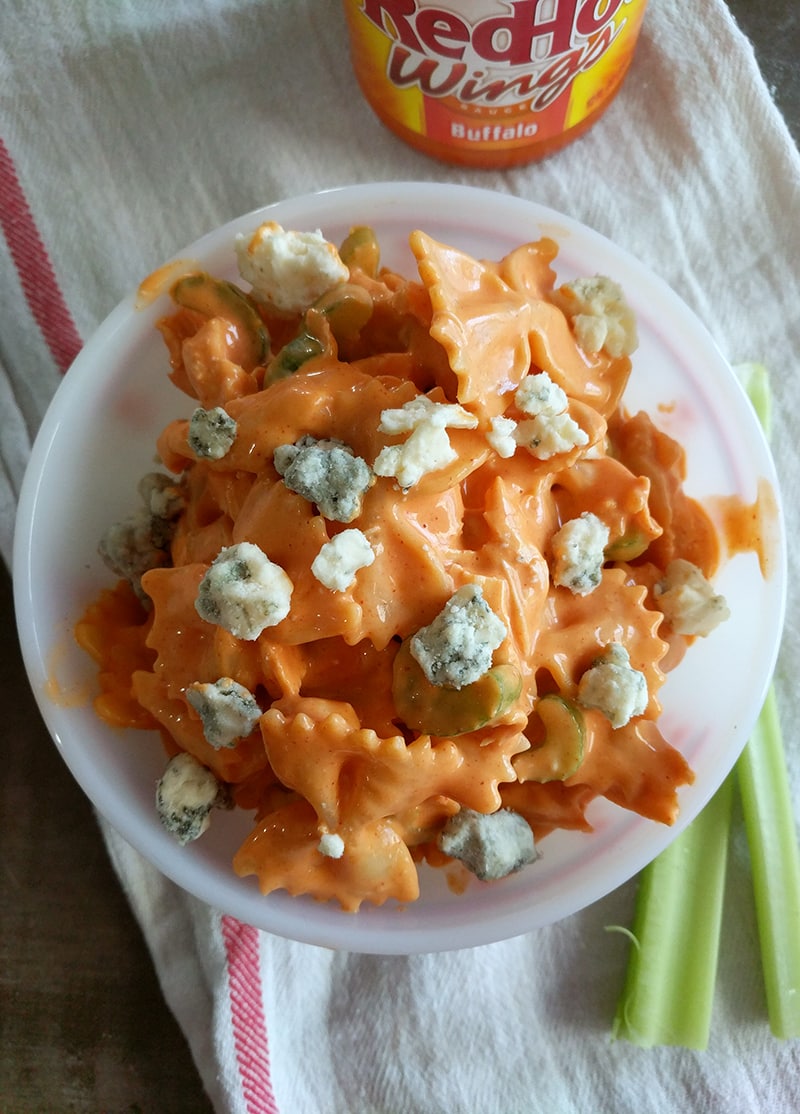 buffalo chicken salad in a bowl with blue cheese on top, celery sticks alongside, and a bottle of RedHot buffalo sauce