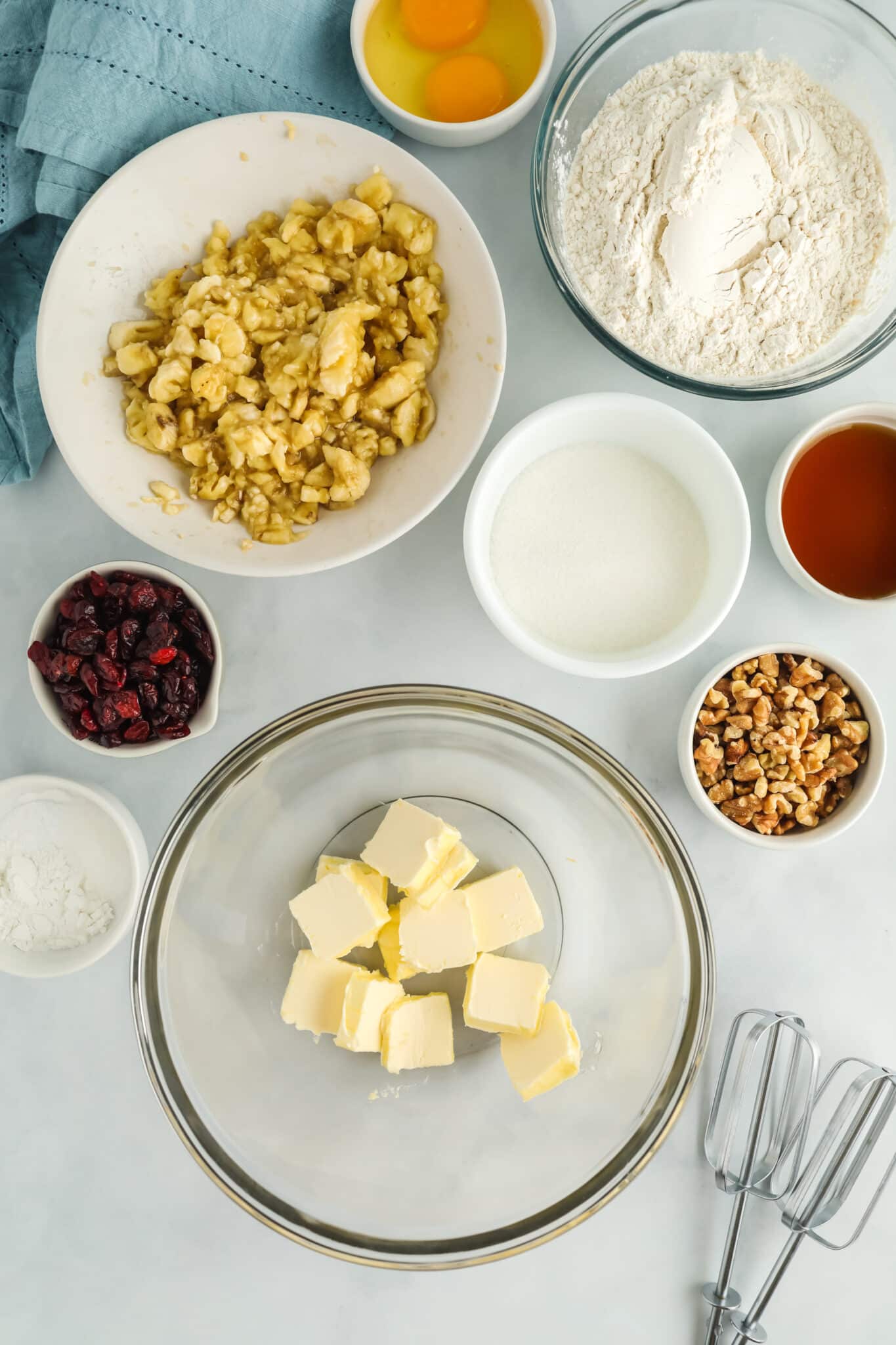 ingredients for banana bread. Including mashed banana, dried cranberry, dry ingredients, butter.