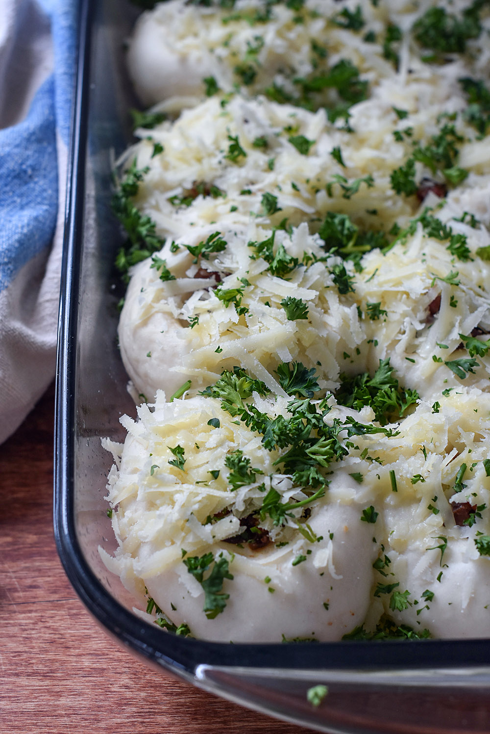 A pan of dinner roll dough topped with cheese, bacon, and parsley ready to be baked.