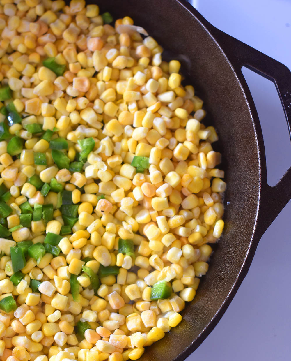 Frozen sweet corn and diced jalapeno in a cast iron pan getting ready to be made into Mexican Street Corn Dip.